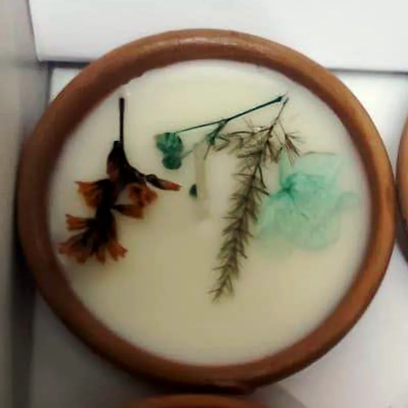 Diya 1: a rust-orange blossom, a feathery fern sprig, tiny turquoise buds and a sea-green petal pressed into white wax in a terracotta bowl.